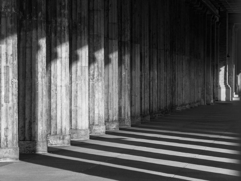 Moody black and white photo of architectural columns and shadows, representing the tone of documentary films by Kemal Bitanga.